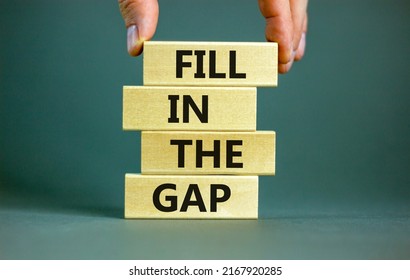 Fill in the gap symbol. Concept words Fill in the gap on wooden blocks on a beautiful grey table grey background. Businessman hand. Business, motivational and fill in the gap concept.