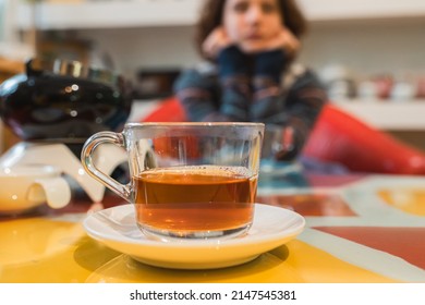 Filled Cup Of Tea On Table. Tea Cafe, Cozy Place To Spend Your Leisure Time, Warm Up With Hot Drink In Cold Weather. Teen Girl In Warm Sweater In Background Out Of Focus