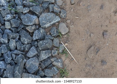 filled frame split in half detailed close up wallpaper background shot of a pile of dark grey gravel ballast stones on one side and brown beige dusty sand and earth ground surface on the other 