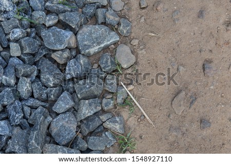 filled frame split in half detailed close up wallpaper background shot of a pile of dark grey gravel ballast stones on one side and brown beige dusty sand and earth ground surface on the other 