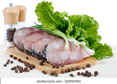 Fillet of fresh raw fish carp on a cutting board with herbs lettuce, green onions and spices. Isolated on white