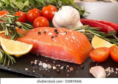 Fillet Of Salmon, Chili Pepper, Lemon Slice And Tomato Over On Black Stone Slate. Healthy Food Concept.