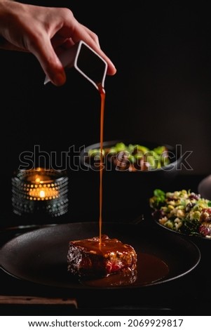 fillet steak on the dark background on the table in restaurant fine dining dinner, man hand sauce pouring over the meat, tasty food around , romantic atmosphere with candle