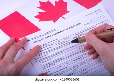 Filling Application (female hands and wood pen) form for Canadian Citizenship - Adults. Immigration, Refugees and Citizenship Canada on Canadian flag surface. 