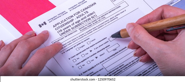 Filling Application (female Hands And Wood Pen) Form For Canadian Citizenship - Adults. Immigration, Refugees And Citizenship Canada On Canadian Flag Surface. 