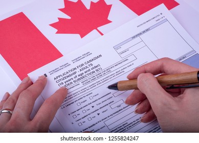 Filling Application (female Hands And Wood Pen) Form For Canadian Citizenship - Adults. Immigration, Refugees And Citizenship Canada On Canadian Flag Surface. 