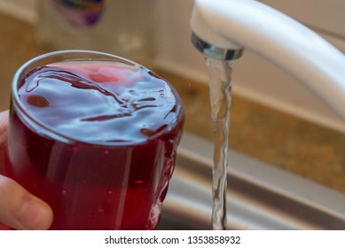 Filling Up A Drink Of Blackcurrant Cordial Juice With Water From A Running Kitchen Sink Tap