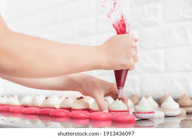 Filling macarons with ganache cream and fruit jam. Close up cropped shot of hands of female confectioner, squeezing red fruit jam into the ganache cream on macarons shells - Powered by Shutterstock