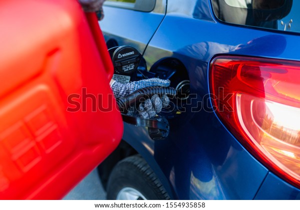 Filling the machine from the canister into the\
neck of the fuel tank. Man pouring fuel into the gas tank of his\
blue car from a red petrol\
canister.
