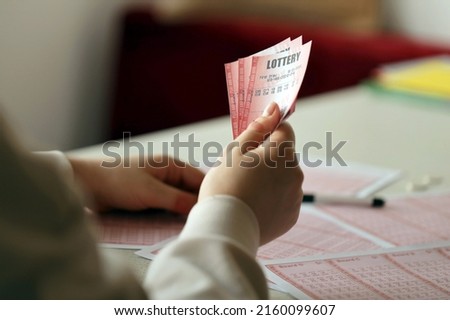 Filling out a lottery ticket. A young woman holds the lottery ticket with complete row of numbers on the lottery blank sheets background. Gambling concept