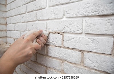 Filling The Seams In A Decorative White Stone In The Form Of A Brick On The Wall. Laying Decorative Stone On The Wall