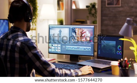 Film maker pointing at the monitor in home office while working on post production for a movie. Video editor wearing headphones.