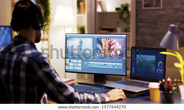 Film maker pointing at the monitor in home\
office while working on post production for a movie. Video editor\
wearing headphones.