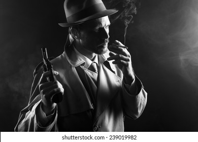 Filmnoir: attraktiver Gangster in Grabenmantel, der eine Zigarette raucht und einen Revolver hält