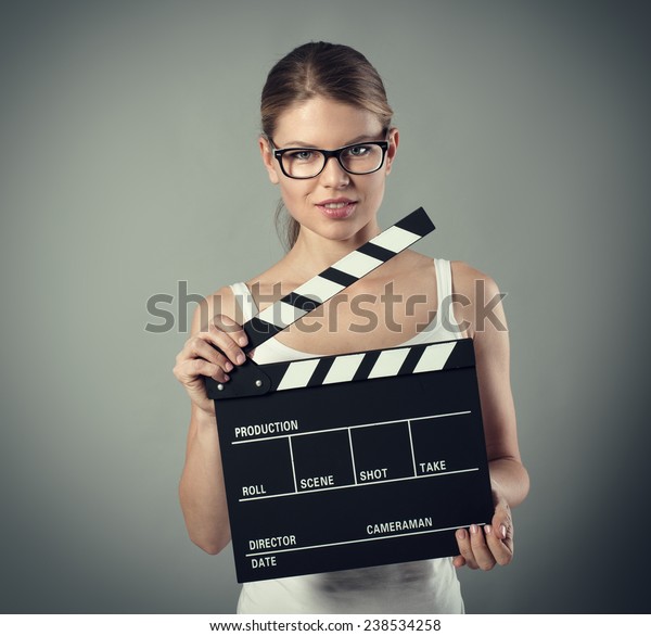 Film production and\
media. Scene tryout. Pretty smiling female with clapperboard over\
grey background.