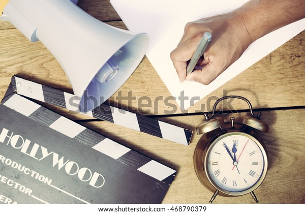 Film production process. Planning to make\
movie. Clapperboard, megaphone, piggy bank, mobile phone and alarm\
clock on wooden table\
background