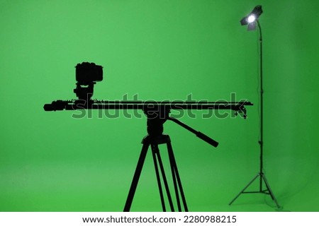Film studio with a green screen. Tripod with camera, and rails. Shooting studio with green room. Chromakey green background.