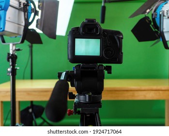 Filming set up with a camera, lights and a green screen 
