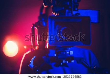 A filmmaker sets up a professional camera while colorful lights illuminate the studio, creating a dynamic atmosphere for shooting.