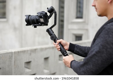 filmmaking, hobby and creativity concept - close up of professional male videographer shooting video using modern dslr camera on 3-axis gimbal over concrete building
