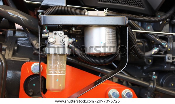 Filter water trap tractor. Fuel filter water trap\
and protective metal frame on tractor parts background with copy\
space. Selective focus