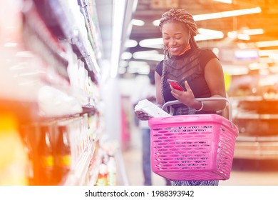 filtered image of excited african lady with shopping bag, smart phone in the hand in a shopping center- 