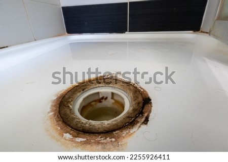 Filthy shower waste in white shower tray surrounded by dirty unhygienic soap scum and black mould
