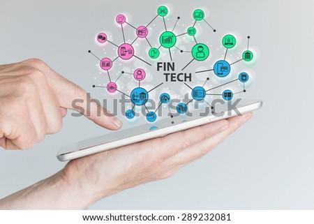 Fin Tech and mobile computing concept. Hand holding tablet with network of financial information technology objects in front of grey background. 