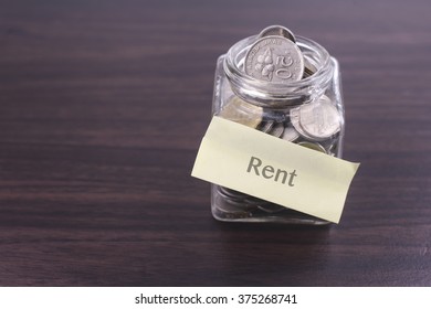 Finacial Concept. Money In The Glass On Wooden Table With Rent Word And Copy Space Area.