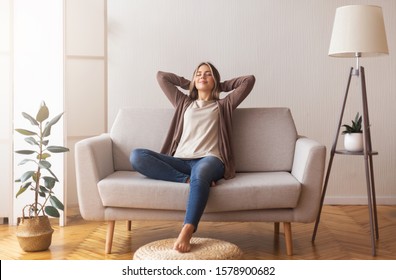 Finally weekends. Millennial girl relaxing at home on couch, enjoying free time, empty space