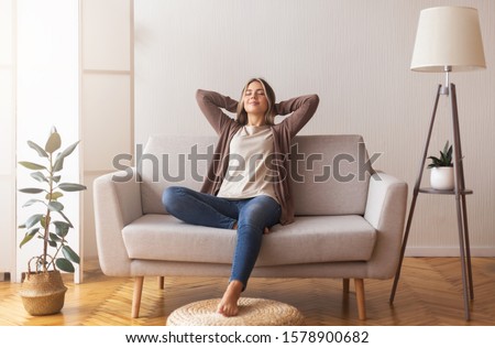 Finally weekends. Millennial girl relaxing at home on couch, enjoying free time, empty space