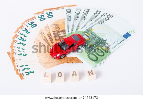 Finance and car loan, saving money for a car or\
material design concepts. Red car on euro banknotes. Money for car\
loan payment on white background. Wooden cubes with word loan. Copy\
space for text.