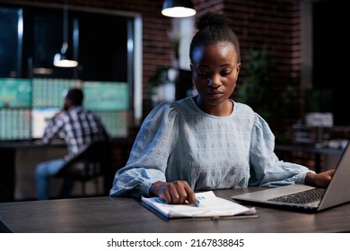 Finance company sales representant reviewing market trend documentation while sitting at desk in office at night. Forex stock agent analyzing financial charts while looking at paperwork clipboard.
