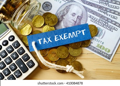 Finance conceptual image with TAX EXEMPT words, hundred dollar bills, golden coins and calculator on wooden background.
