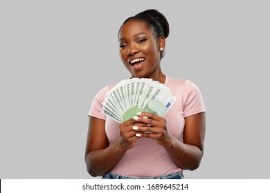 Finance, Currency And People Concept - Happy African American Young Woman Holding Hundreds Of Euro Money Banknotes Over Grey Background