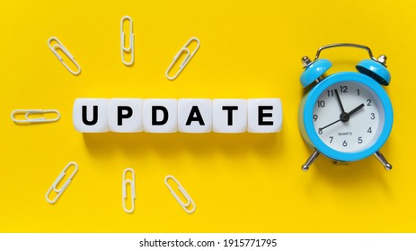 Finance and economics concept. On a yellow background, a blue alarm clock, paper clips and white cubes on which the text is written - UPDATE - Shutterstock ID 1915771795