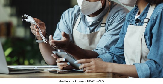 Finance, Small Business, COVID-19 Pandemic. Sad Millennial African American Couple Owners Of Small Business In Protective Masks Work With Laptop And Smartphone And Accounts In Cafe, Cropped, Panorama