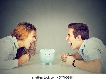 Finances In Divorce Concept. Wife And Husband Can Not Make Settlement Screaming Piggy Bank In-between Sitting At Table Looking At Each Other With Hatred
