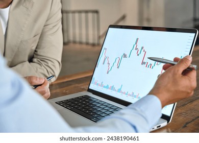 Financial advisor explaining invest stock market data consulting investor. Two business men analysts doing finance trading analysis pointing at chart on laptop screen working in office. Close up. - Powered by Shutterstock