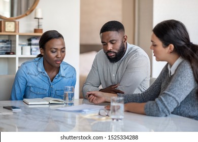 Financial advisor going over a savings plan with a young African American couple while sitting at a table in their living room at home