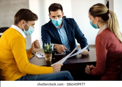 Financial advisor going through paperwork with a couple in the office and wearing face mask due to COVID-19 pandemic.