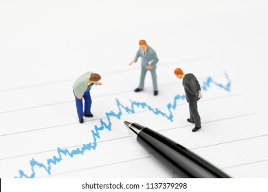 Financial analysis, investment consultant or advisor concept, miniature professional businessmen standing and looking, review on volatility blue stock market line graph data report with pen. - Powered by Shutterstock