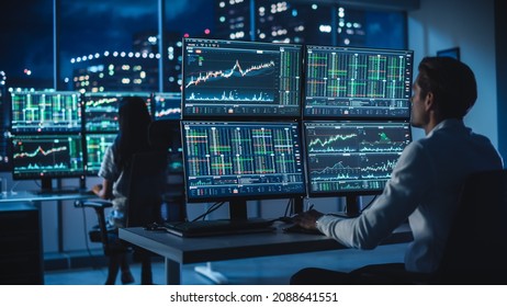 Financial Analyst Working on a Computer with Multi-Monitor Workstation with Real-Time Stocks, Commodities and Foreign Exchange Charts. Businessman Works in Investment Bank City Office at Night. - Powered by Shutterstock