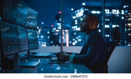 Financial Analyst Working on Computer with Multi-Monitor Workstation with Real-Time Stocks, Commodities and Exchange Market Charts. African American Businessman Works in Investment Bank Late at Night. - Powered by Shutterstock