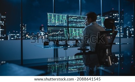 Financial Analyst Working on a Computer with Multi-Monitor Workstation with Real-Time Stocks, Commodities and Exchange Market Charts. Businessman Works in Investment Bank Downtown Office at Night.