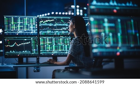 Financial Analyst Working on a Computer with Multi-Monitor Workstation with Real-Time Stocks, Commodities and Exchange Market Charts. Businesswoman at Work in Investment Broker Agency Office at Night.