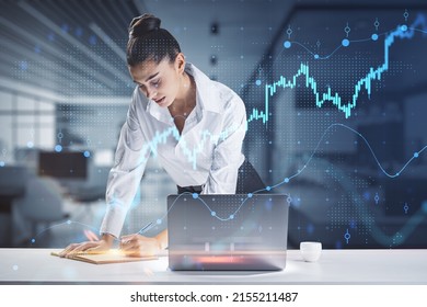 Financial analyzing and market forecast concept with young woman working with data, making notes in notebook and growing digital forex chart diagram and candlestick, double exposure - Powered by Shutterstock