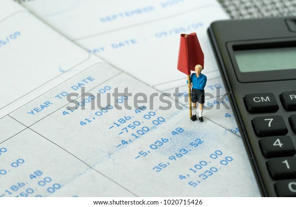 Financial budget, debt, tax or set money\
target concept, miniature figure standing and holding red flag on\
salary slip with black\
calculator.