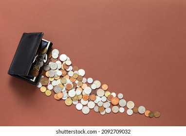 Financial community and prosperity concept. Coins of different countries are poured out of one wallet on brown background. Money flows like river. Empty space for text. Flat lay, top view, copy space