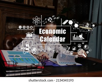 Financial Concept About Economic Calendar With Inscription. Young Finance Market Analyst In Eyeglasses Working While Sitting At Wooden Table On Background.
